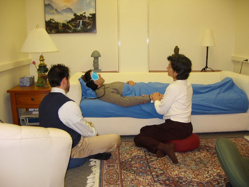 A facilitator supporting a person resting on a couch in a therapeutic session